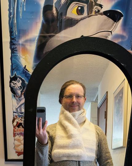 Another mirror selfie with scarf, similar to the first, though the scarf is wound higher, again over the chin and up to the ears, with the extra fuzzy section angling down to the chest. This crop shows the star of the Balto movie looking up and off to the right above the round-topped mirror.