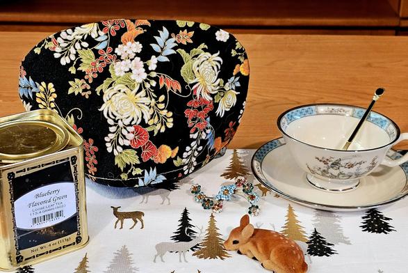 Tea tableau with a deer patterned tea towel, a vintage velour flocked fawn figurine, a floral cozy, and Blueberry green tea.